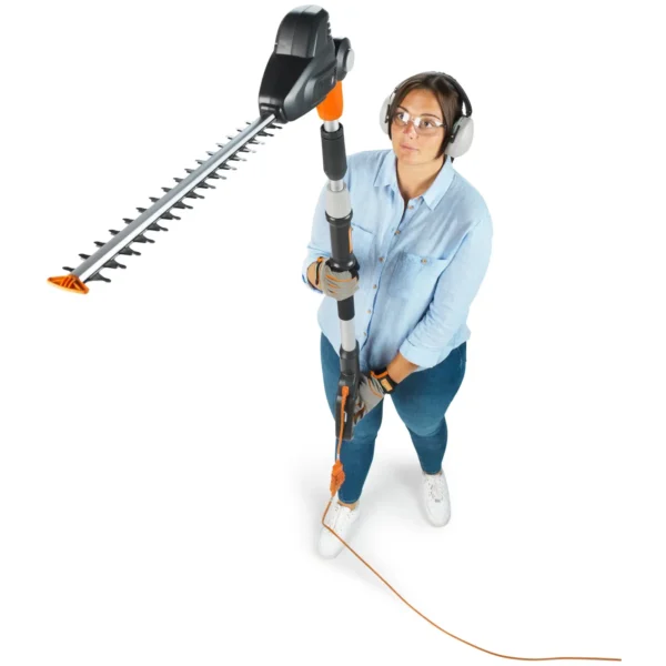 Woman in safety gear operating a long‑reach hedge trimmer, wearing gloves, safety glasses, and headphones.